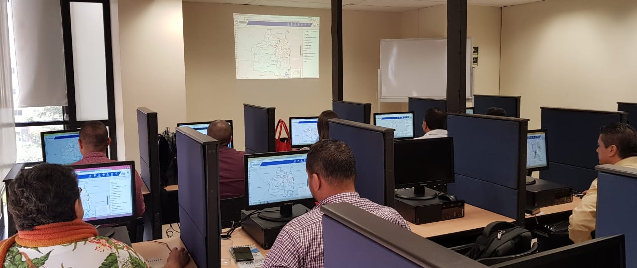 Personas ubicadas en una de las salas de capacitaciones de Comfenalco Valle, sentadas frente a computadores realizando un taller práctico de capacitación en los servicios web geográficos de la IDESC.