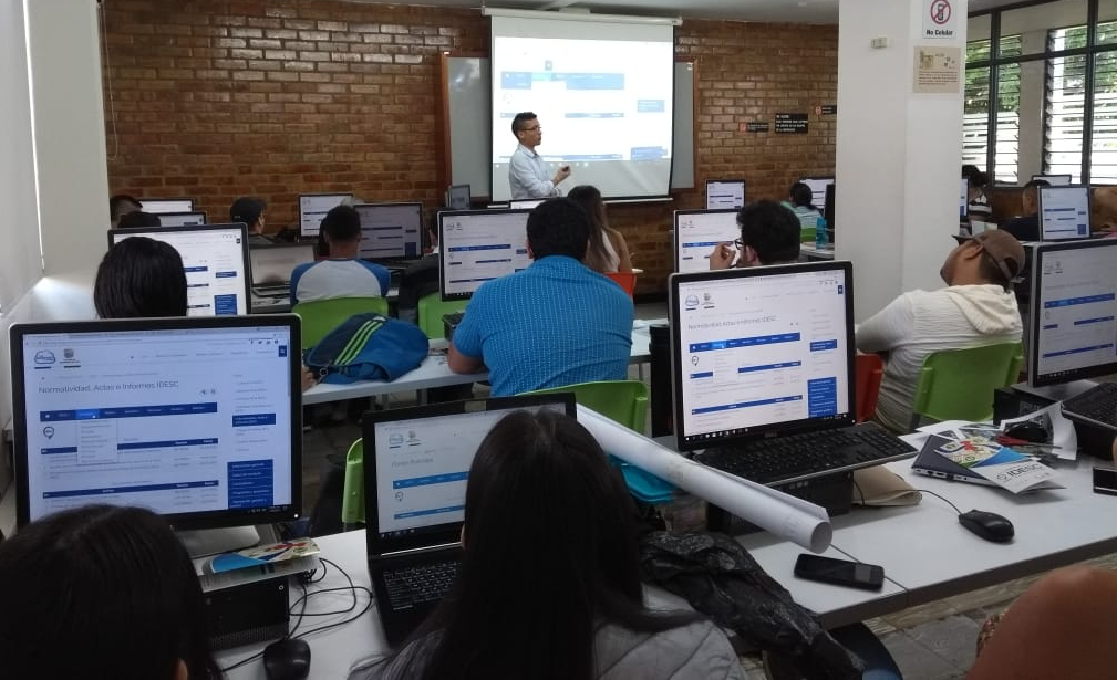 Estudiantes de Arquitectura ubicados en una de las salas de capacitaciones de la Universidad San Buenaventura, sentadas frente a computadores realizando un taller práctico de capacitación en los servicios web geográficos de la IDESC.