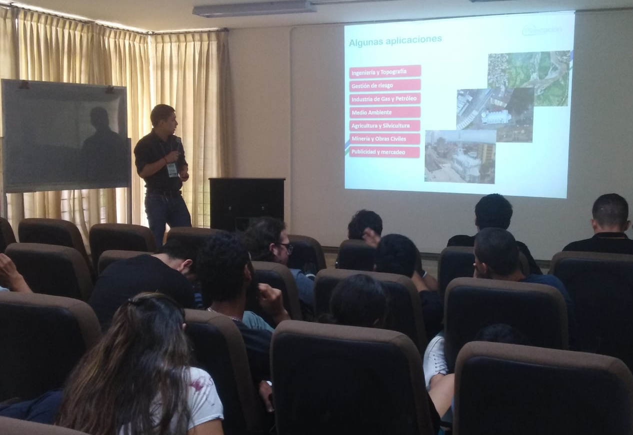 Estudiantes prestando atención a la exposición del representante de la IDESC, en un auditorio localizado en el plan de estudios de Ingeniería Topográfica.